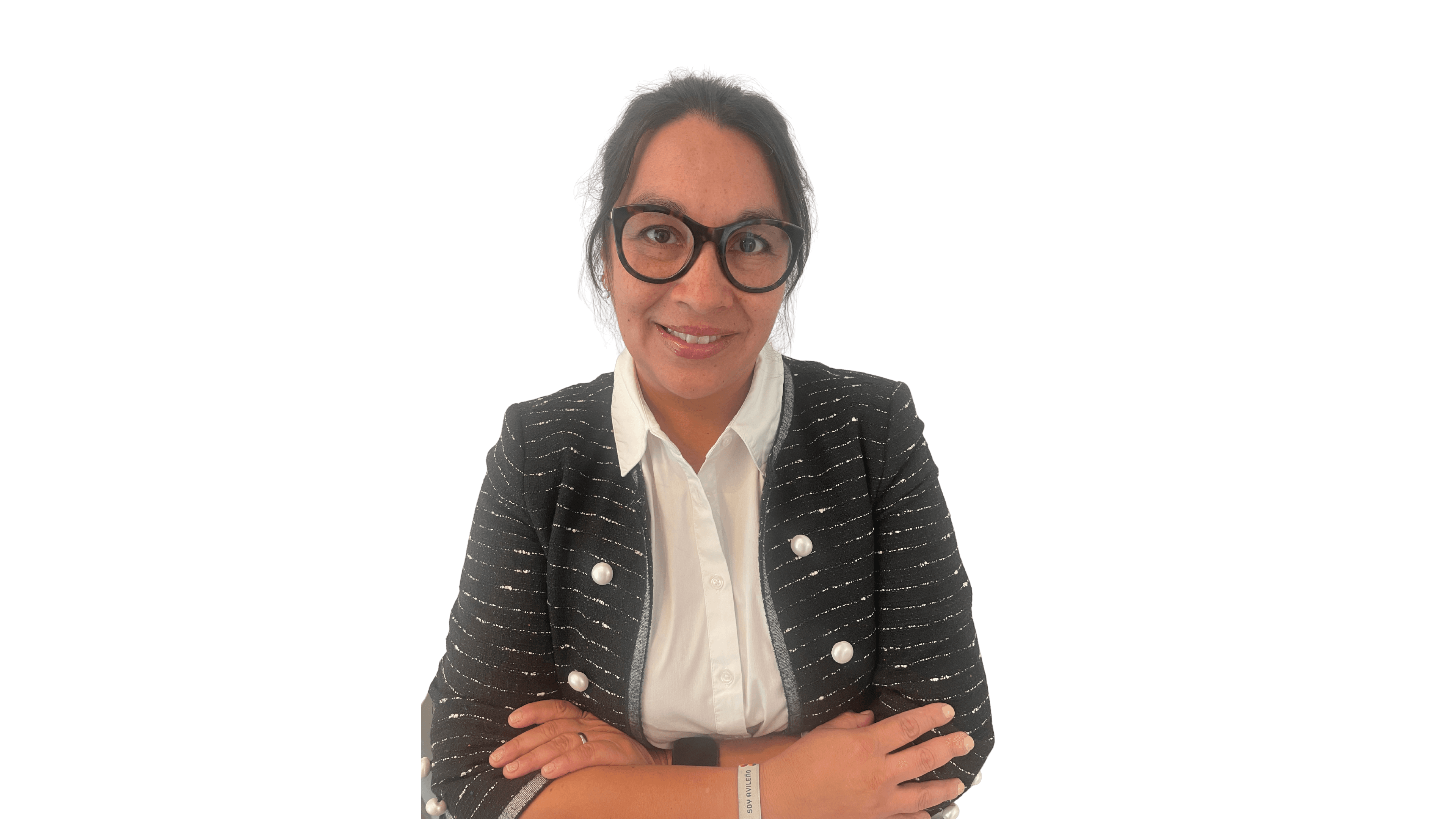 Mujer con gafas y chaqueta oscura con perlas sonríe con brazos cruzados sobre fondo negro.