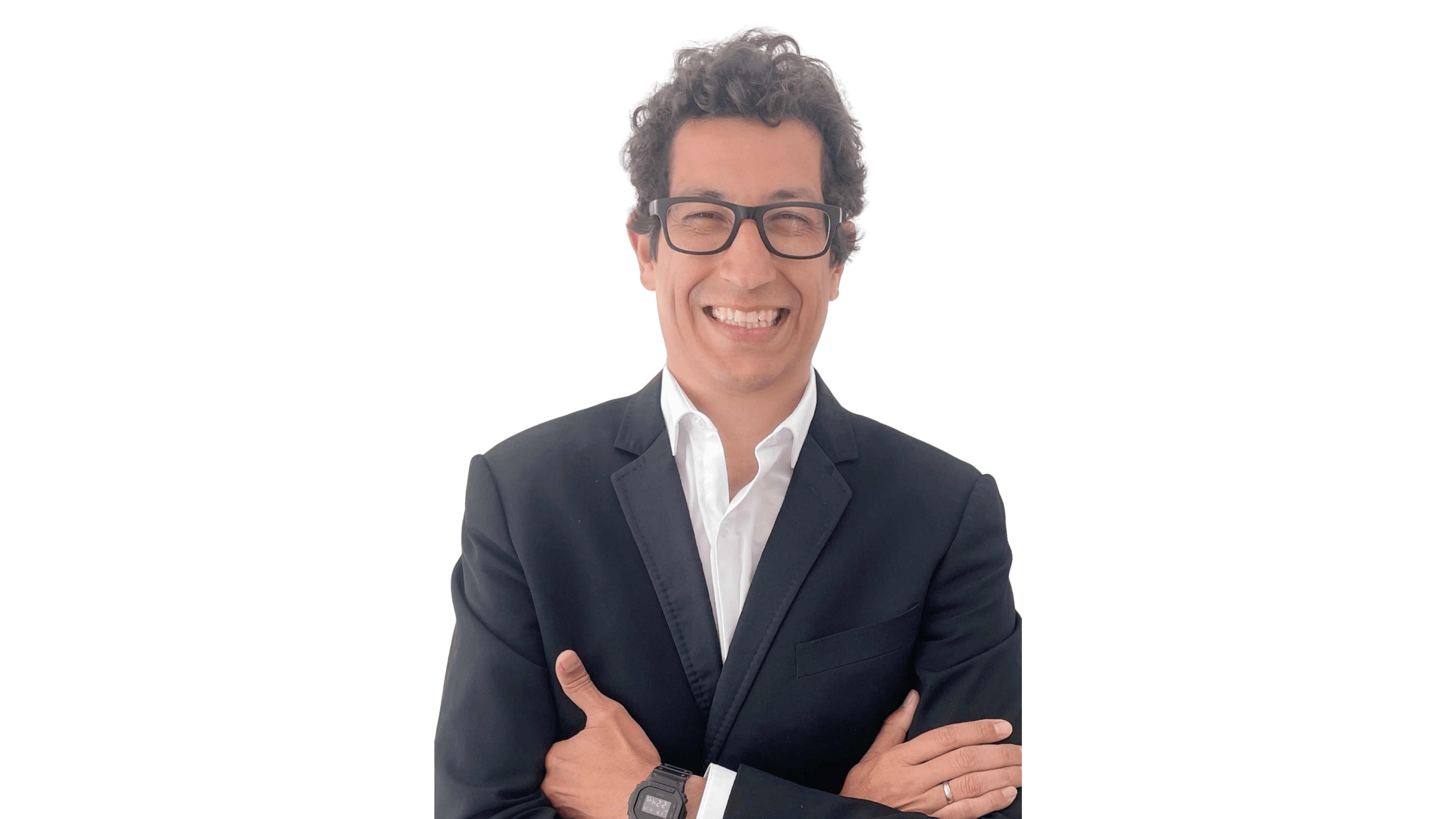 Hombre sonriente con gafas y traje negro posa con brazos cruzados ante un fondo negro.