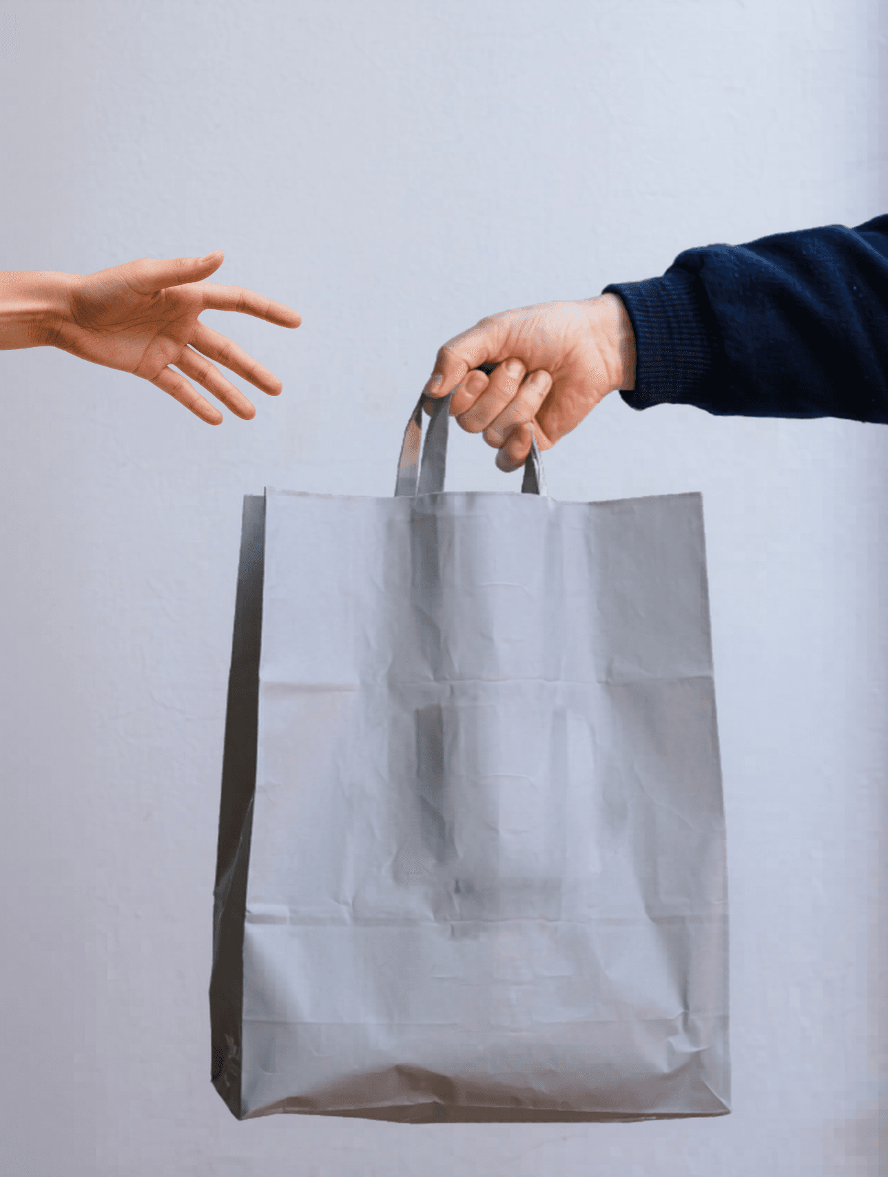 Mano con manga azul entregando una bolsa de papel gris a otra mano extendida.